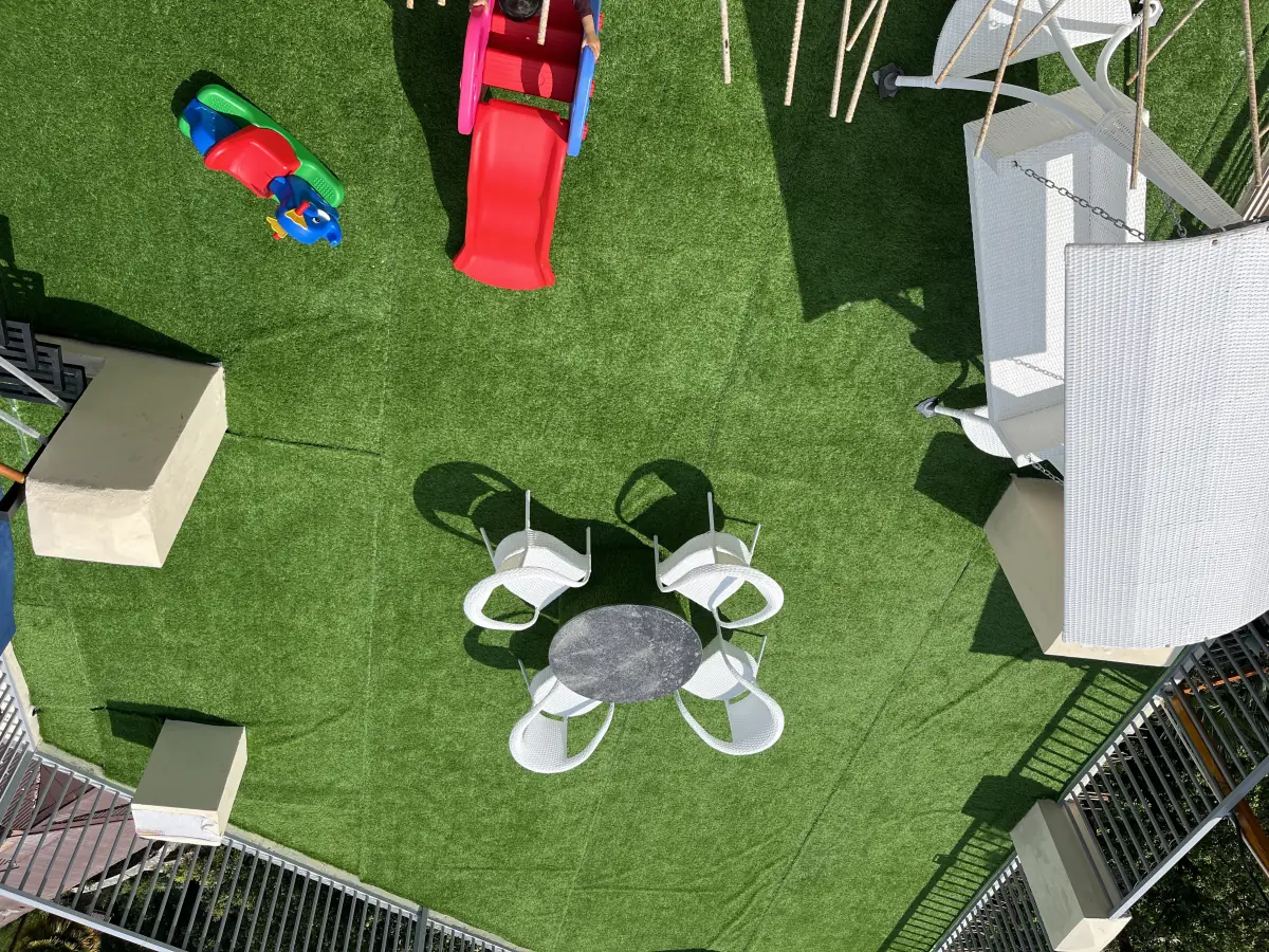 Looking down on the rooftop lawn: white chairs around a round table, with a children's slide and play toys off to one side.